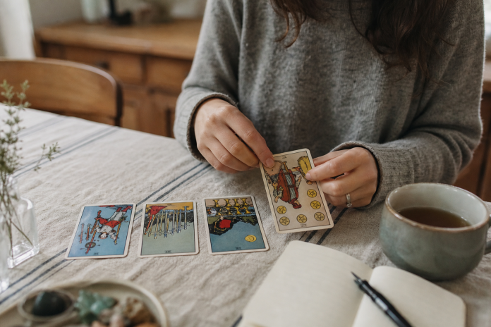 Reading Reversed Tarot Cards: Meanings, Methods and Examples Hands turning over a reversed tarot card on a kitchen table beside three face-up cards, a mug of tea and a notebook