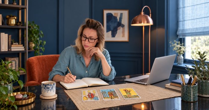 Keep, release, start tarot journaling Woman journaling beside three tarot cards on a camel mat, with a silver laptop to her right.
