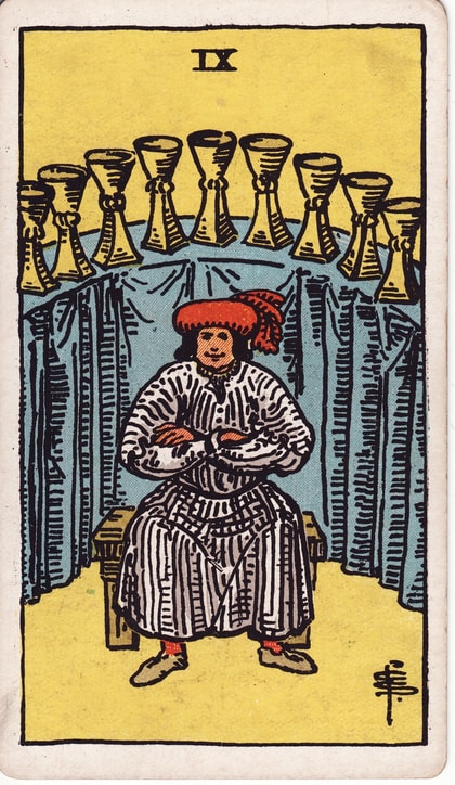 Nine of Cups card: a seated figure in a red cap folds his arms below an arc of nine golden cups on blue cloth.