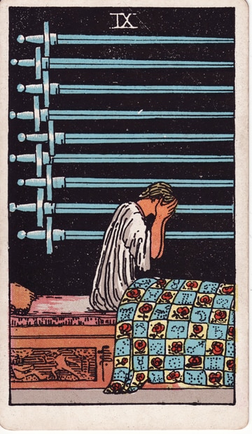 Nine of Swords: a seated figure covers their face below nine blue swords against a dark field, beside a patterned quilt.